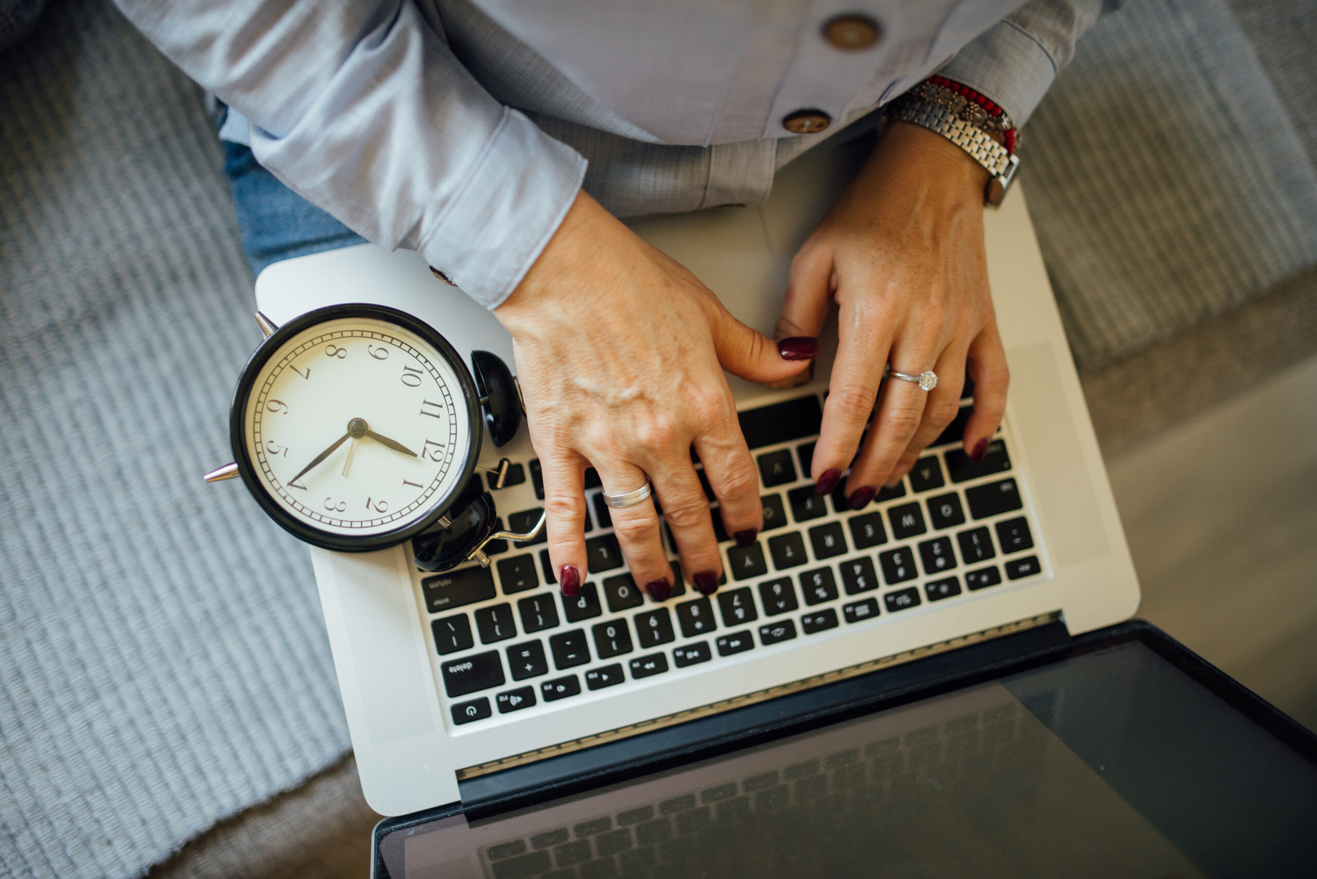 Hands typing on a laptop keyboard against the clock while editing a draft post