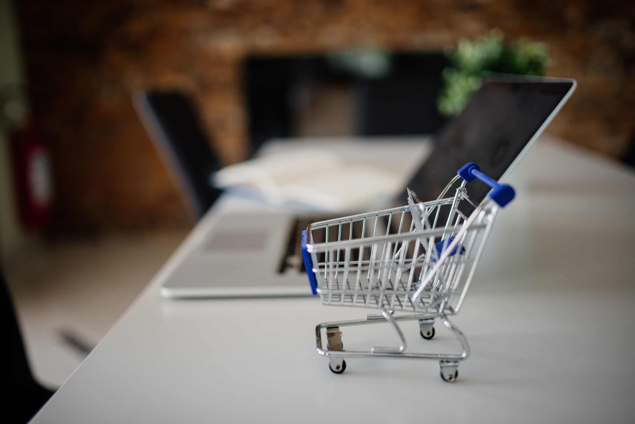 Miniature shopping cart next to a laptop representing affiliate marketing and e-commerce