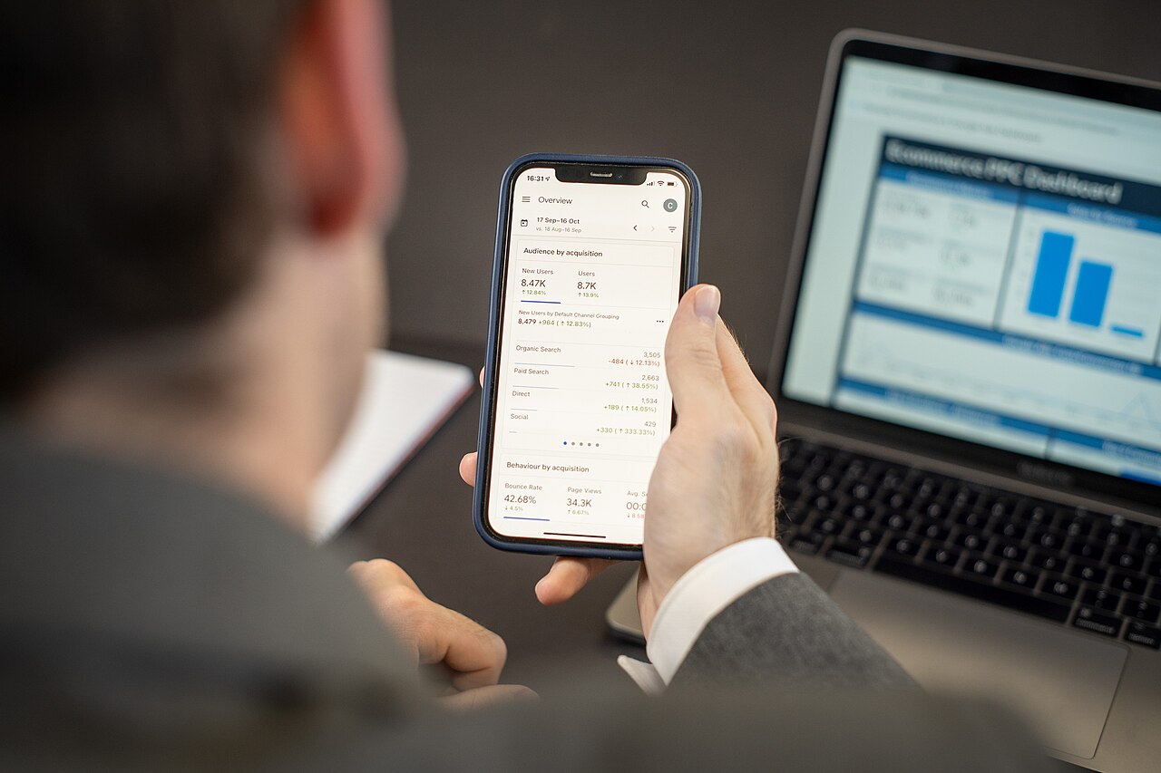 Person checking website analytics on a phone next to a laptop