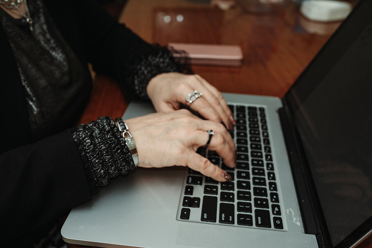 Hands typing on a laptop at a wooden table.
