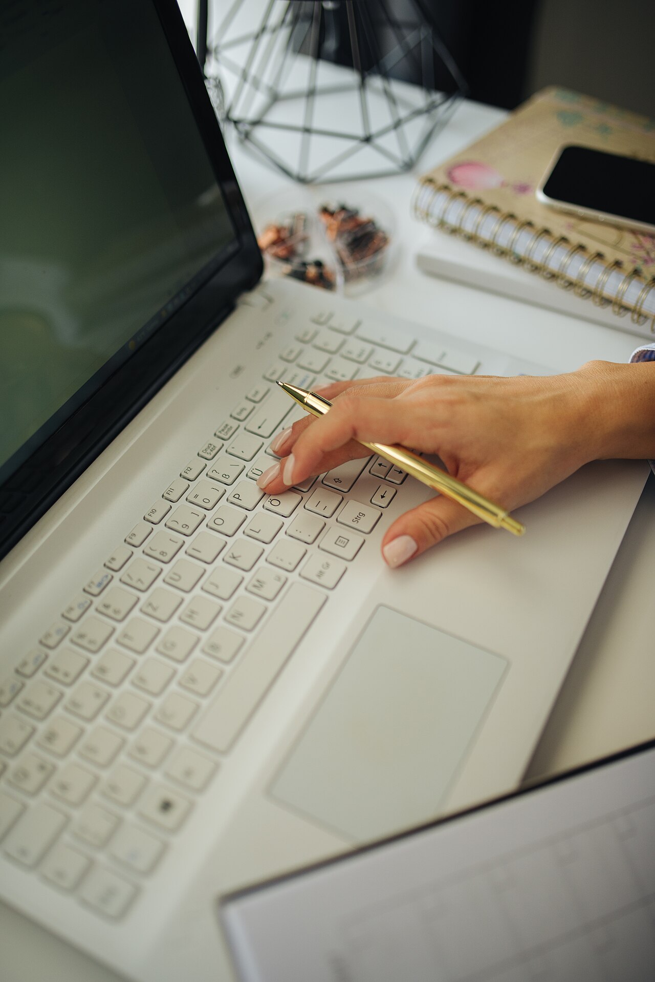 Hand reaching for a pen while working on a laptop surrounded by notebooks