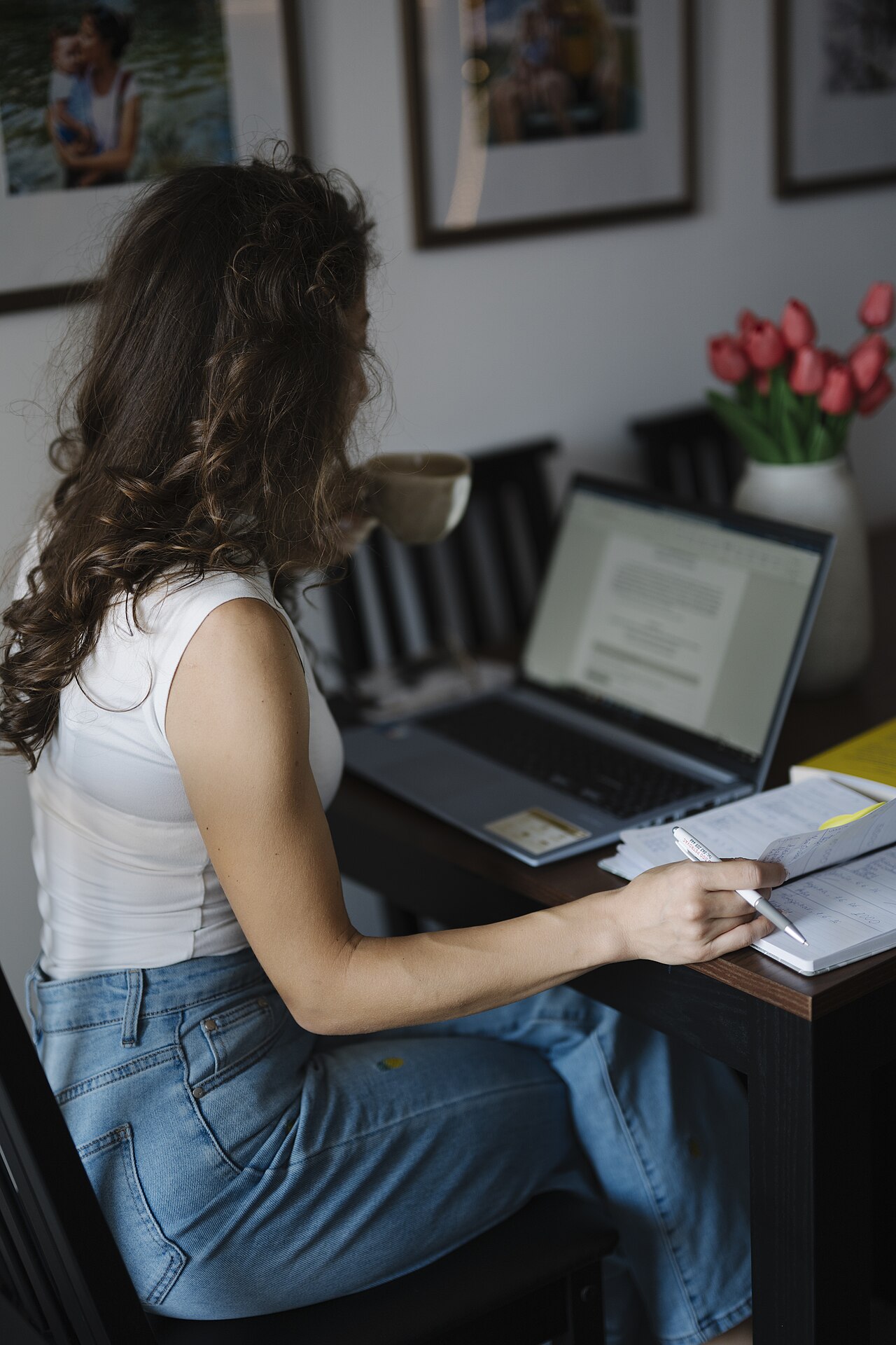 Woman working on a laptop at a desk while holding a cup