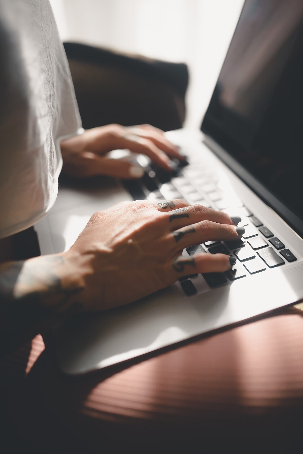 Hands typing an email on a laptop keyboard in warm sunlight